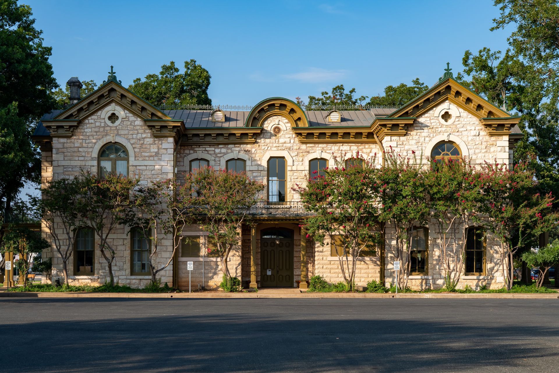 Stone house facade with arched windows, vines, and a central entrance under a blue sky