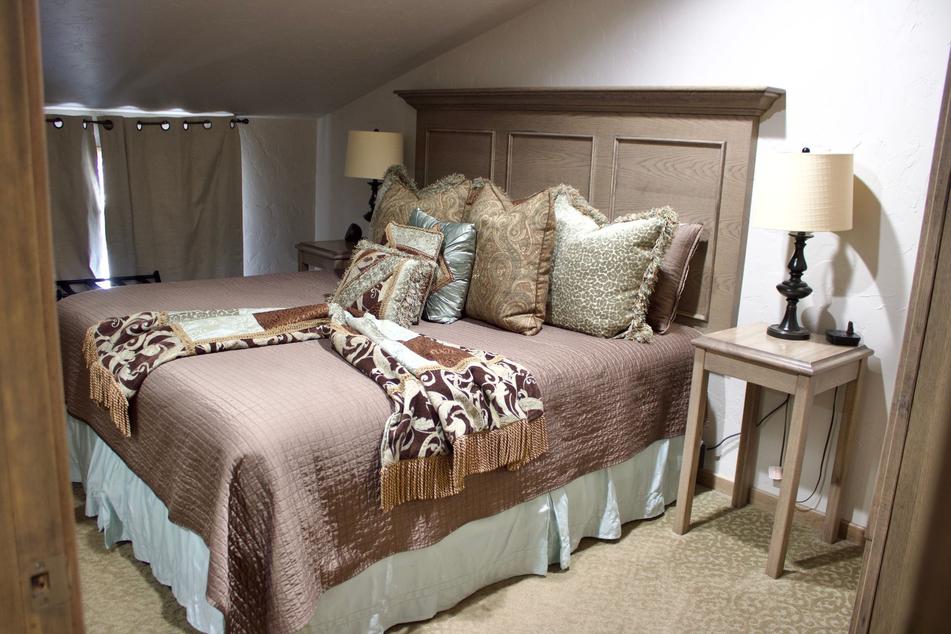 Cozy bedroom with a large bed, patterned bedding, and matching bedside tables in a neutral-toned attic room
