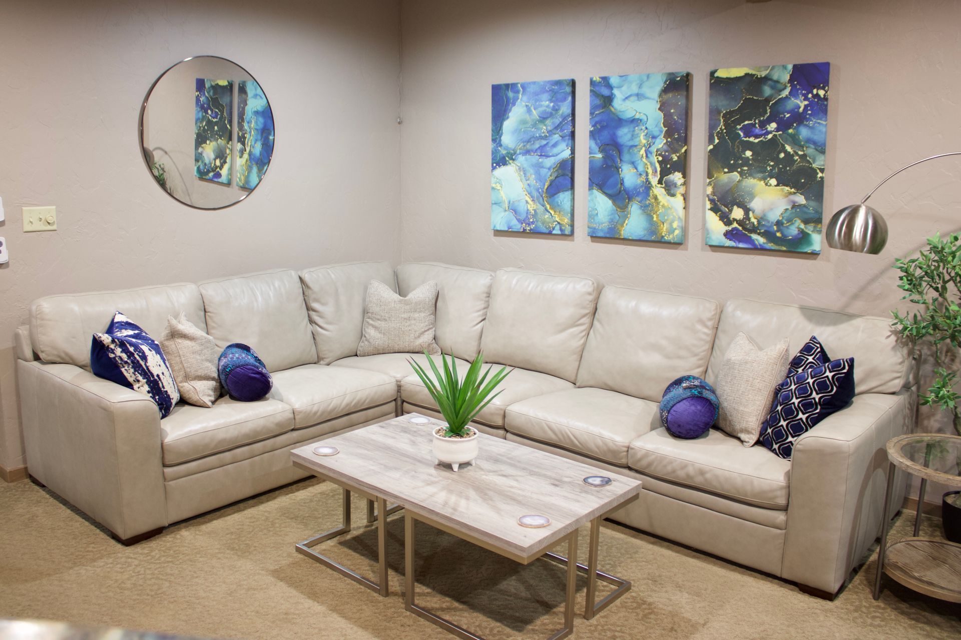 Modern beige sectional sofa with blue pillows, glass coffee table, wall art, and a floor lamp in a living room
