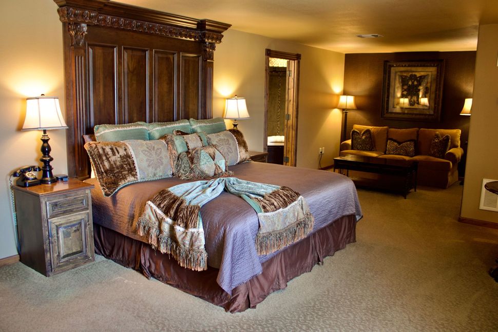 Neatly made bed with dark bedding and cream throw in a cozy bedroom with two bedside lamps and framed art.