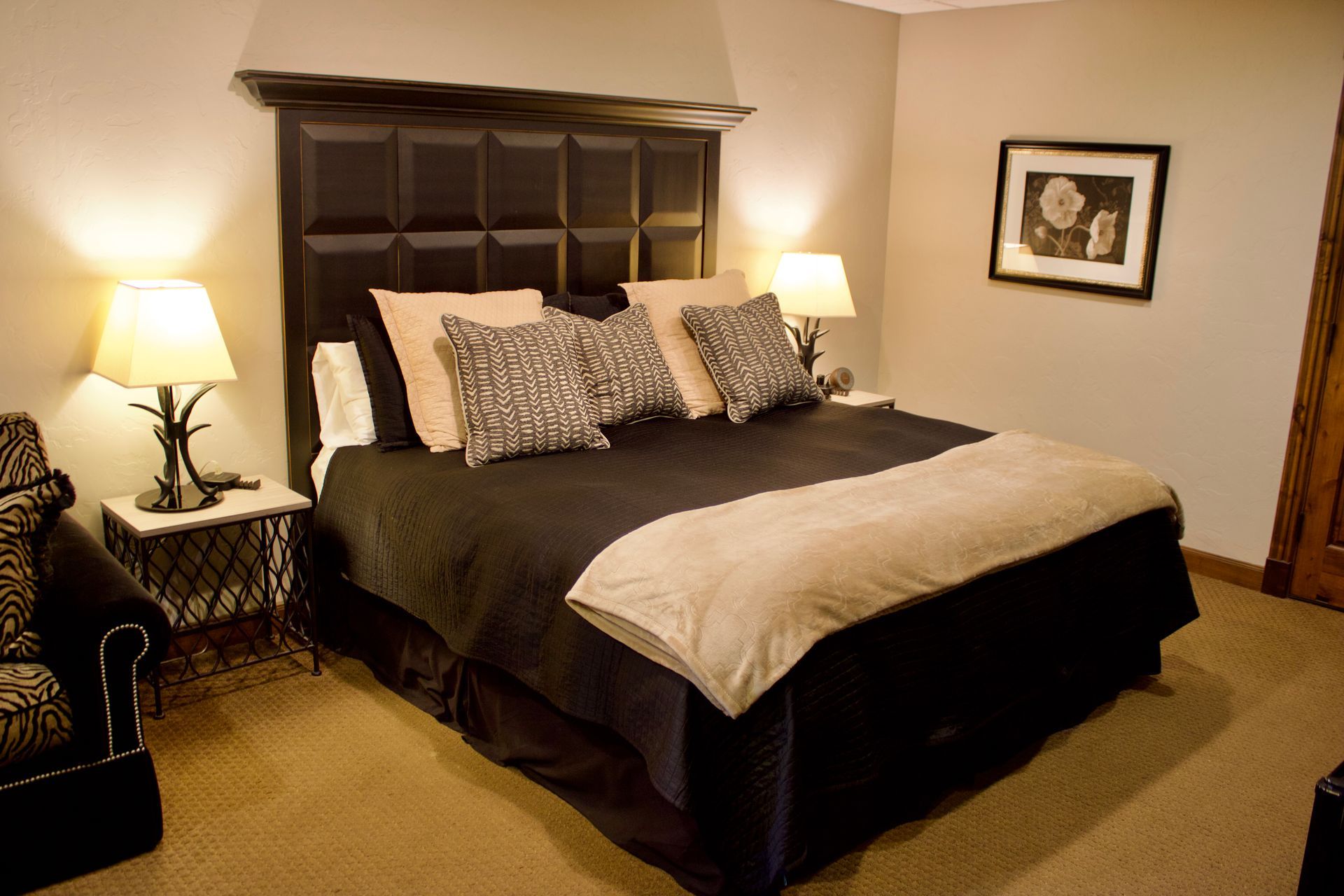 Cozy bedroom with a dark wooden bed, black bedding, white throw, lamps, and framed wall art.
