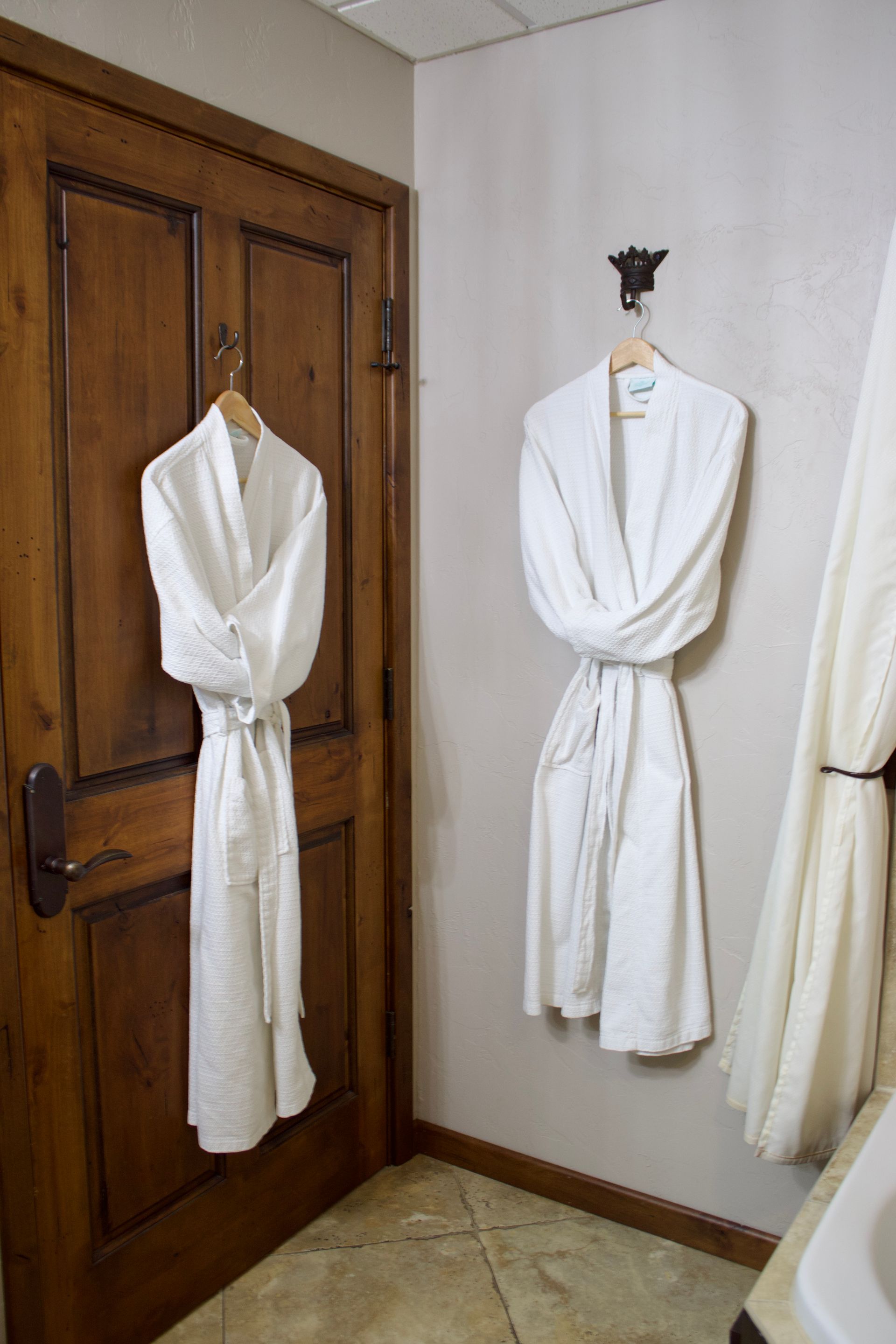 Two white robes hanging on a wooden door and wall hook in a small room.