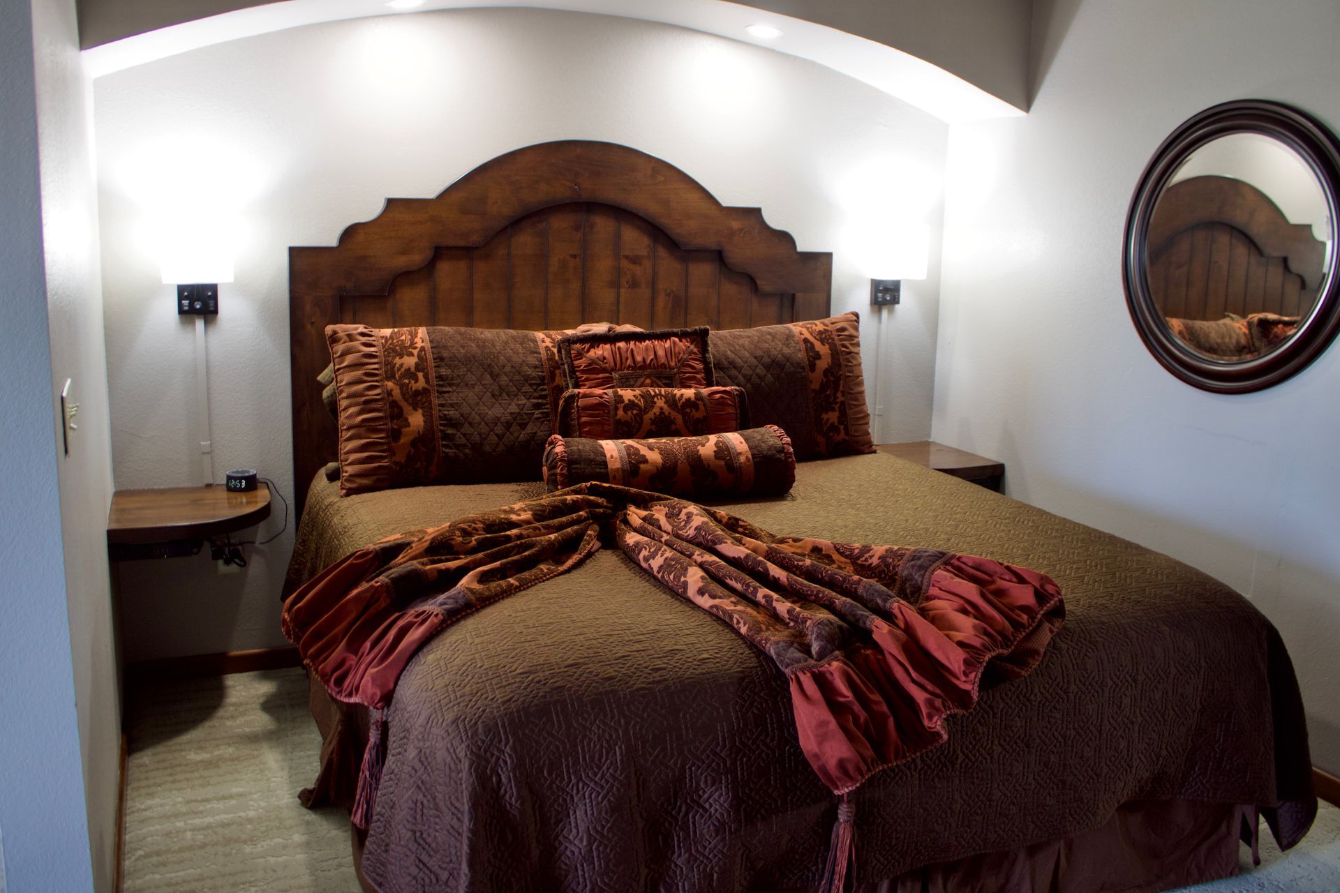 Cozy bedroom with a large bed, patterned brown bedding, arched ceiling, and wall sconces.