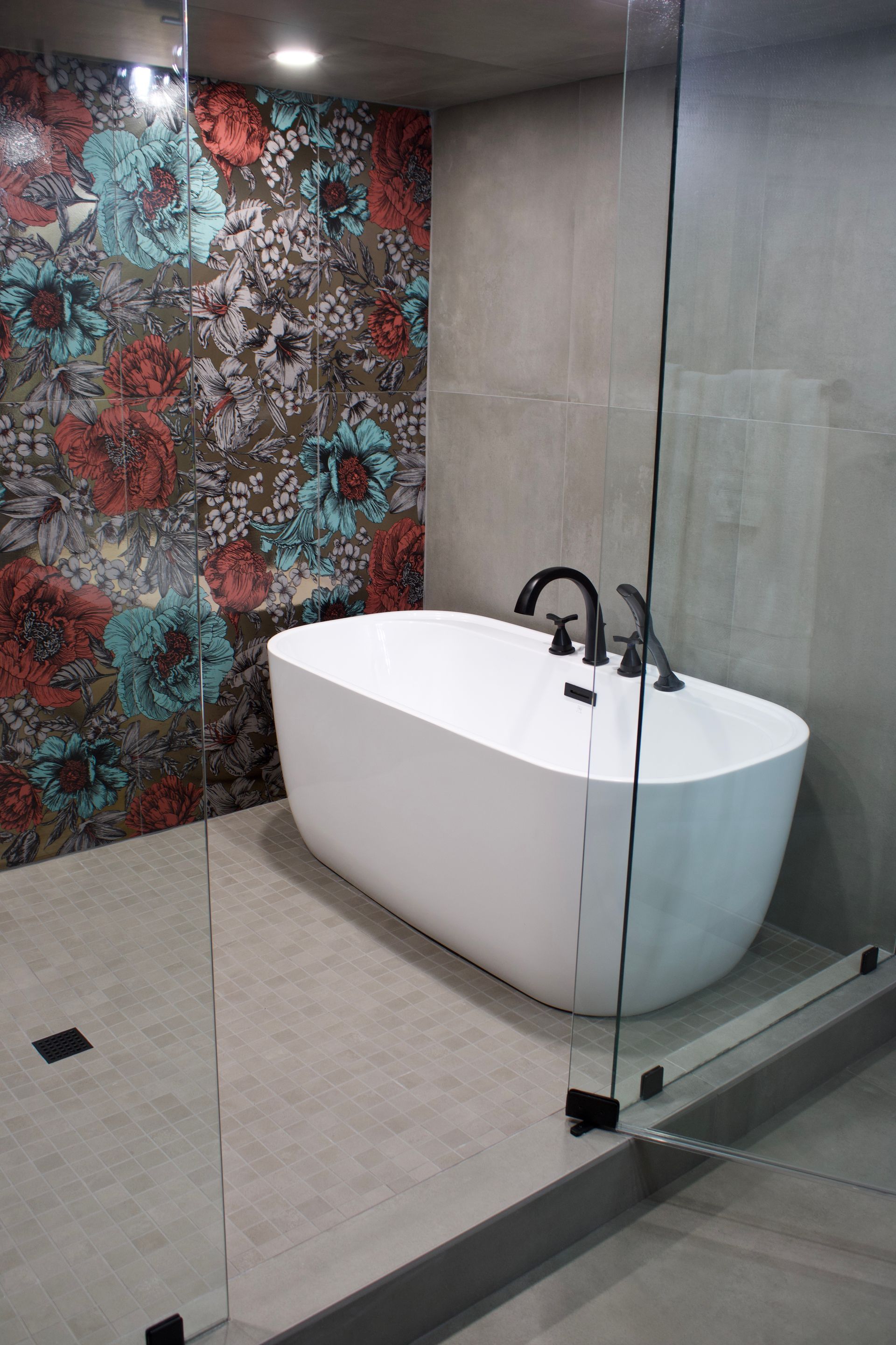 Modern bathroom with a white freestanding tub, glass shower wall, gray tile, and colorful mosaic accent wall