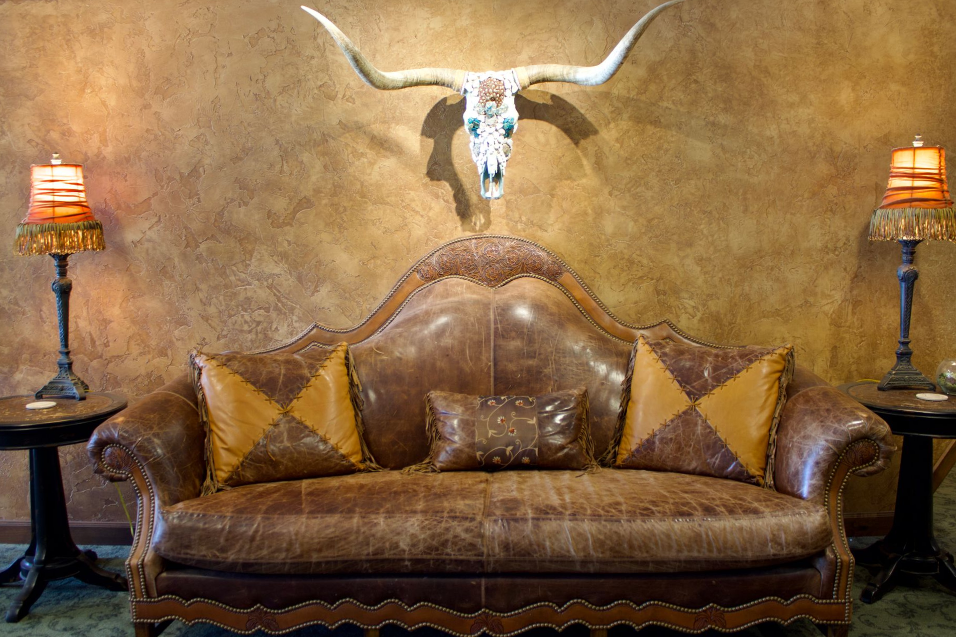 Brown leather sofa with patterned pillows, antelope skull wall decor, and two lit lamps in a rustic room
