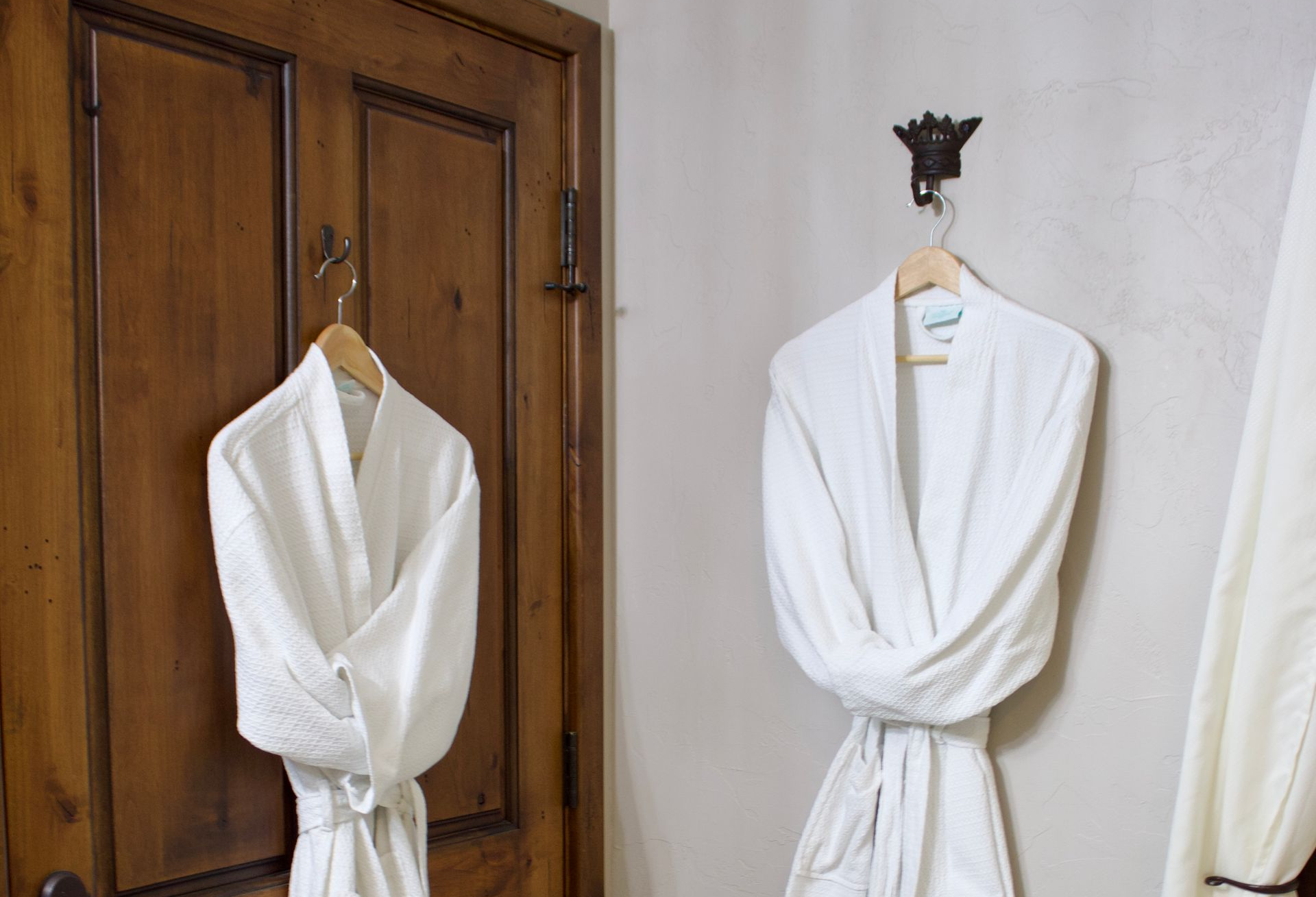 Two white robes hanging on wall hooks beside a wooden door