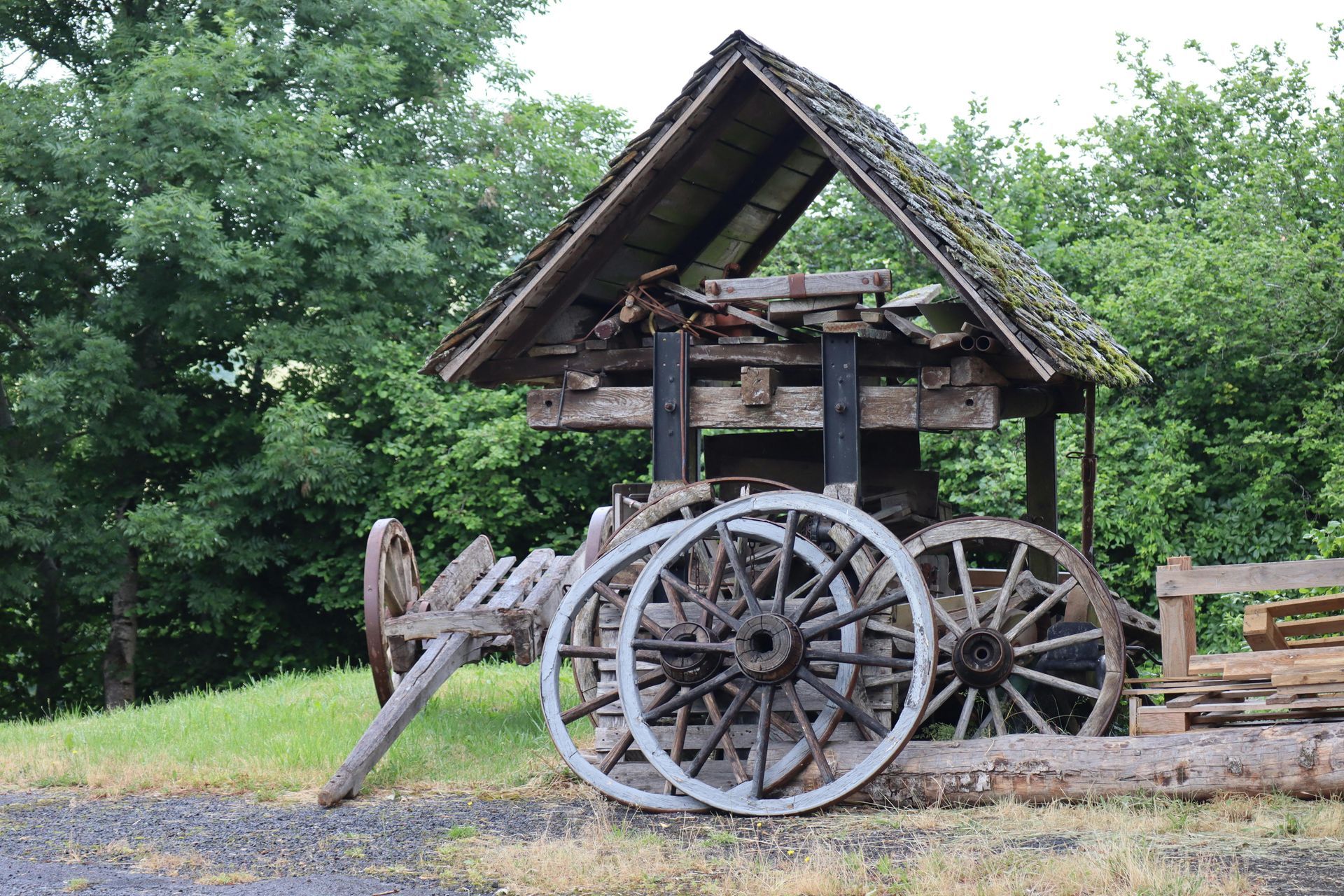 Rusty vintage steam engine wagon under a wooden shelter in a grassy outdoor setting