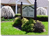 Pepper Funeral Home sign in front of building with bushes and weeping trees.