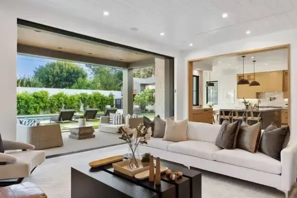 Living room with open sliding doors to patio with pool; white sofa, dark coffee table, green yard.