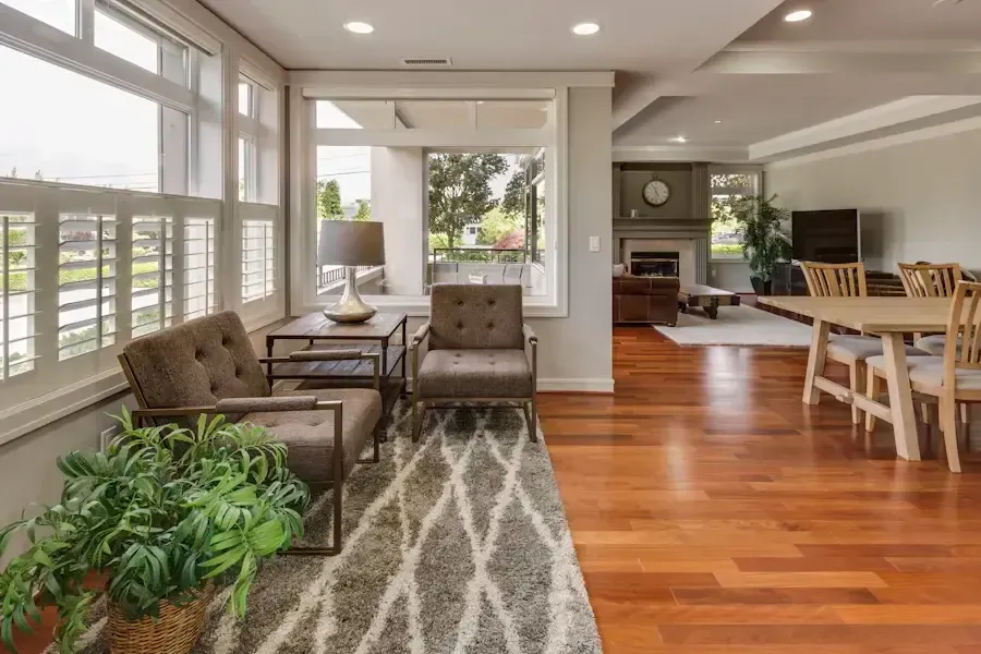 Living room with wood floor, gray rug, armchairs, dining table, and fireplace.