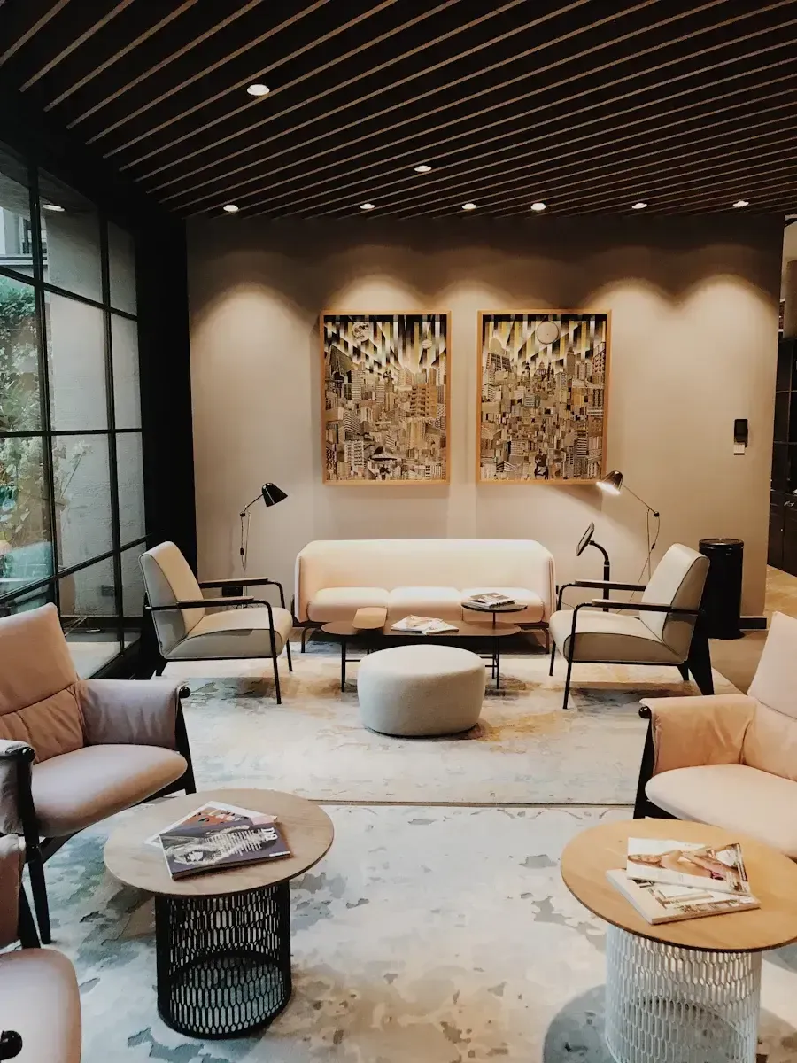 Lounge area with neutral tones: beige sofa, armchairs, coffee tables, artwork, and a wood-slat ceiling.