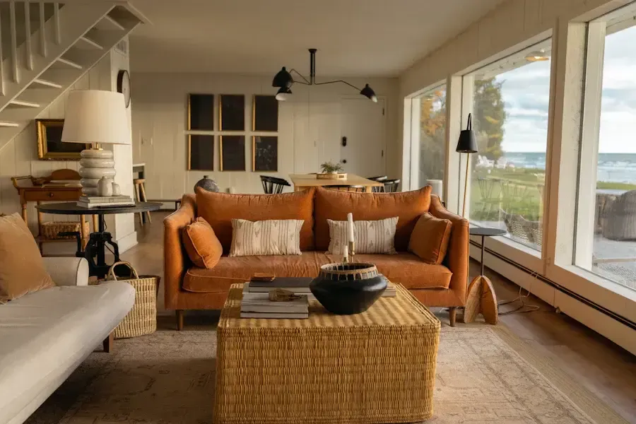 Cozy living room with orange couch, wicker coffee table, and large windows overlooking a lake.