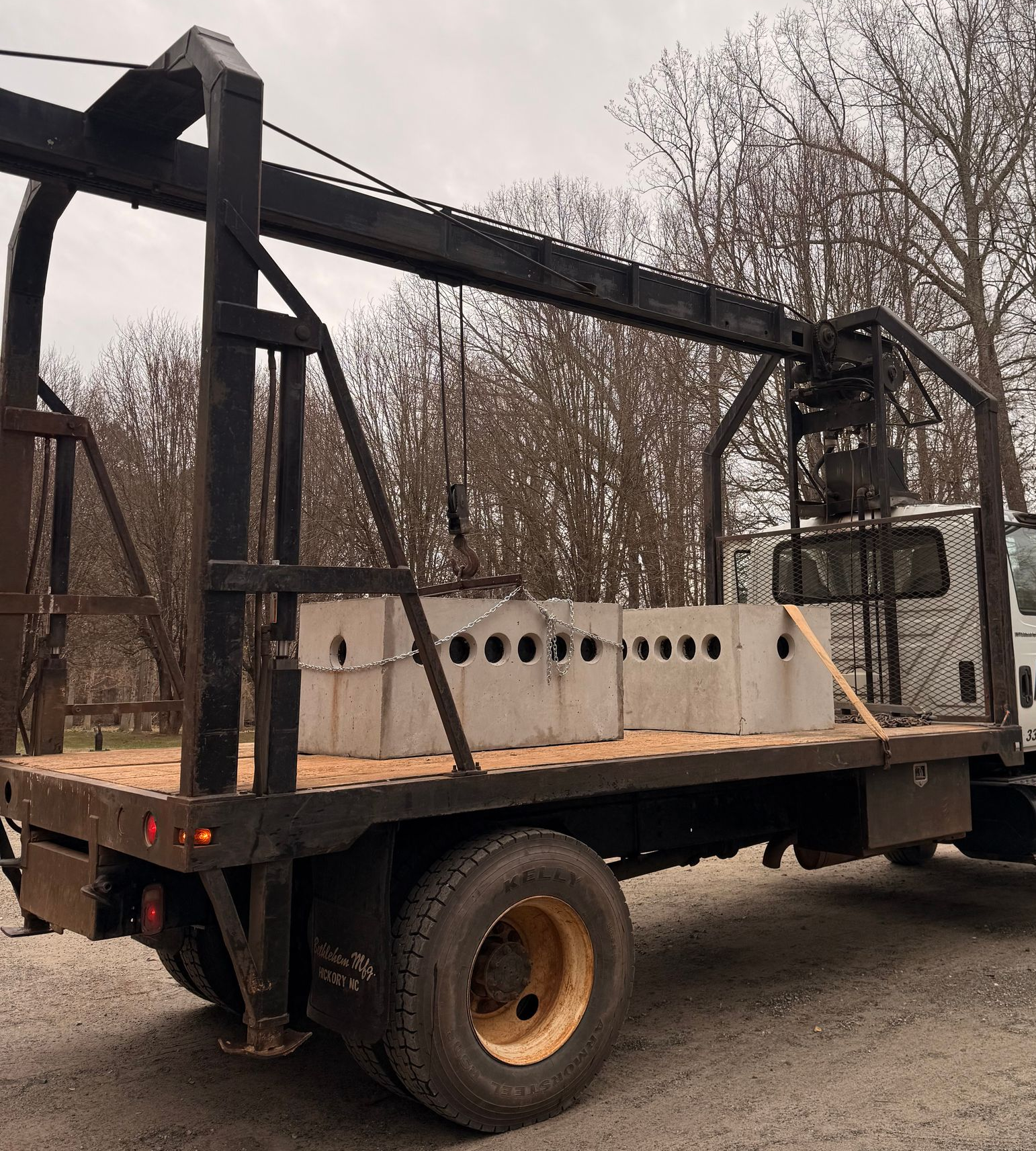 Flatbed truck carrying concrete blocks, equipped with a crane, outdoors.