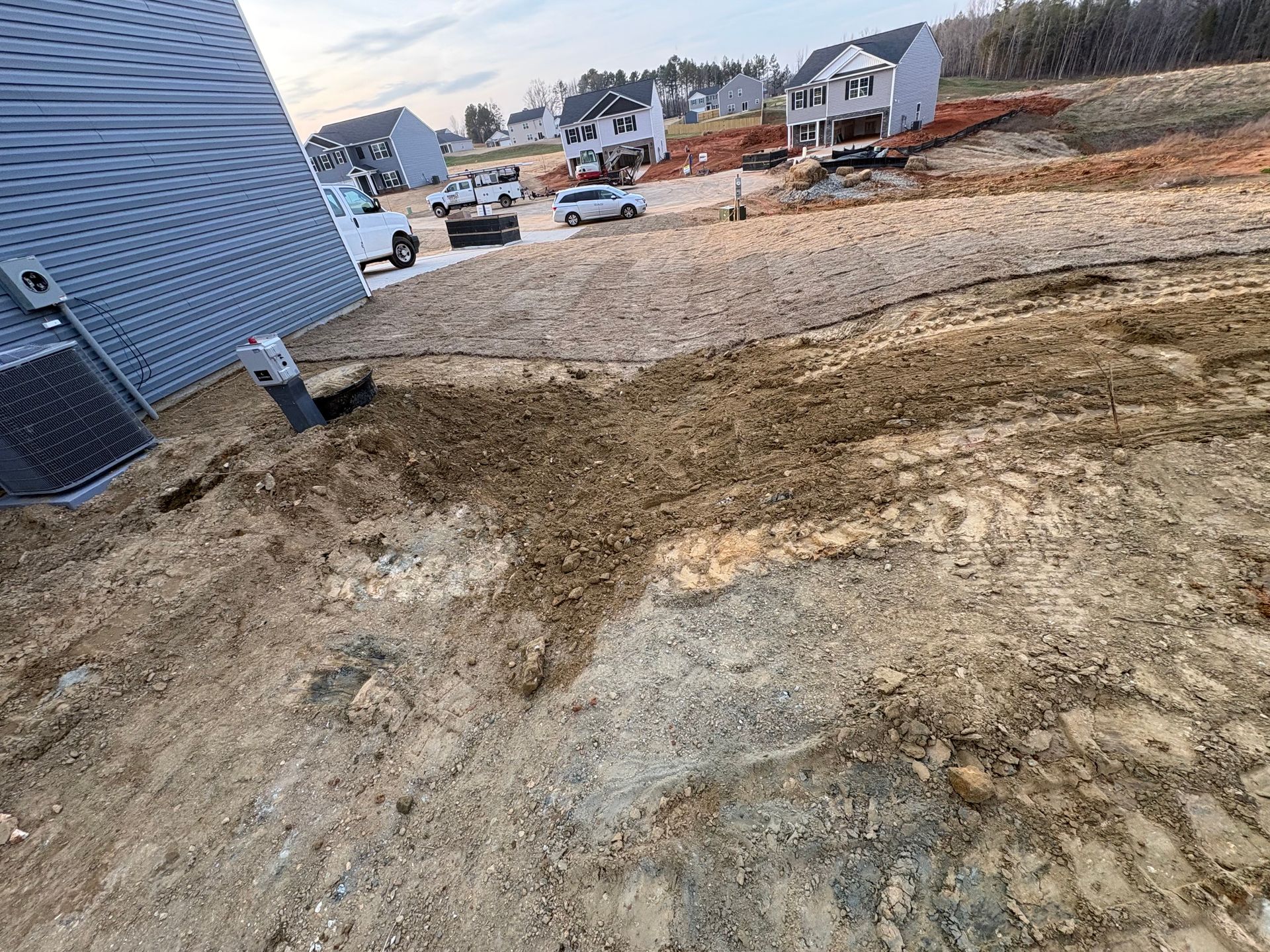 An unfinished yard with exposed brown dirt and tire tracks next to the siding of a new residential house.