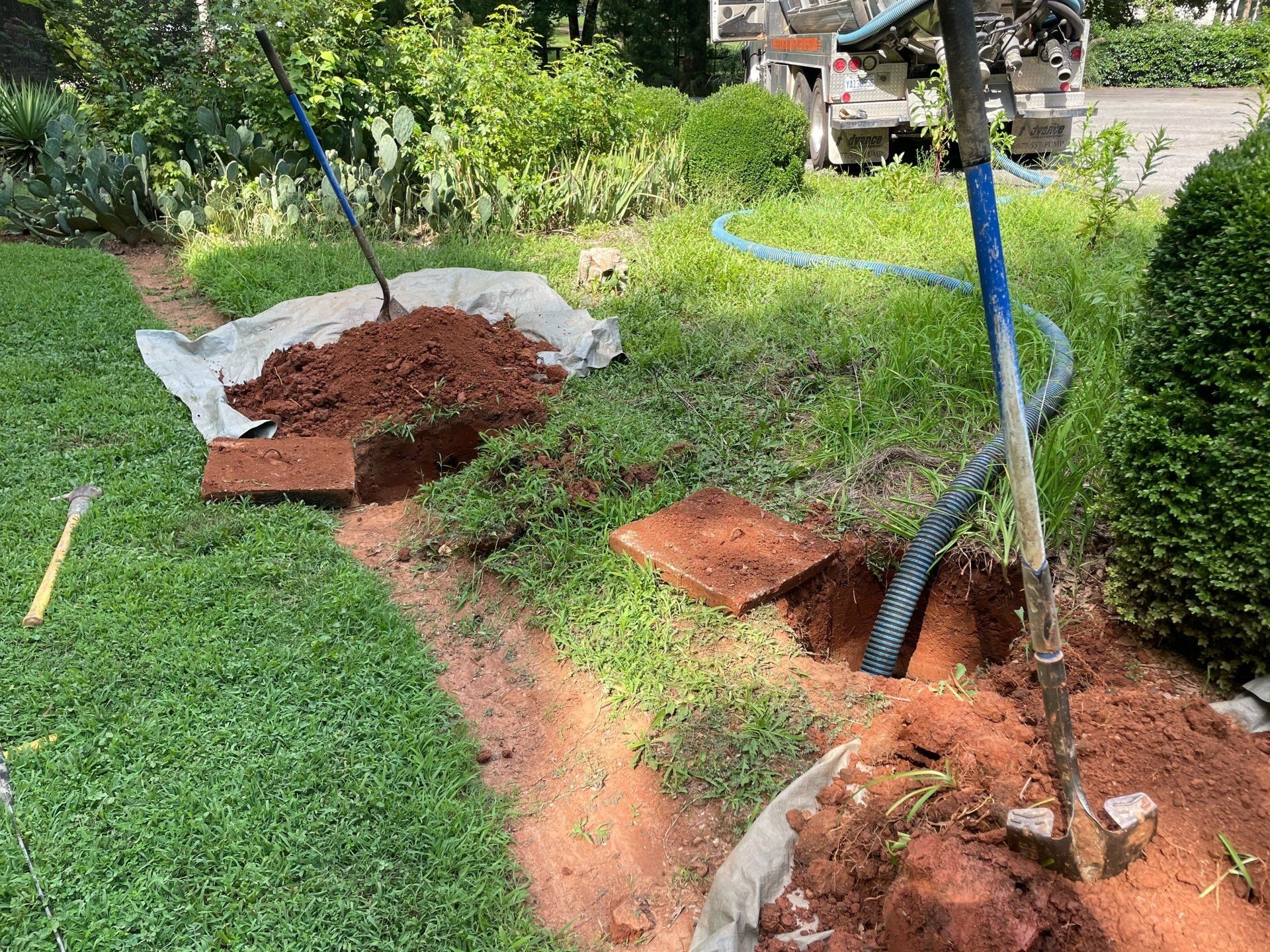 Construction site: digging trenches in lawn, brown soil and tools scattered, hose extends to background truck.