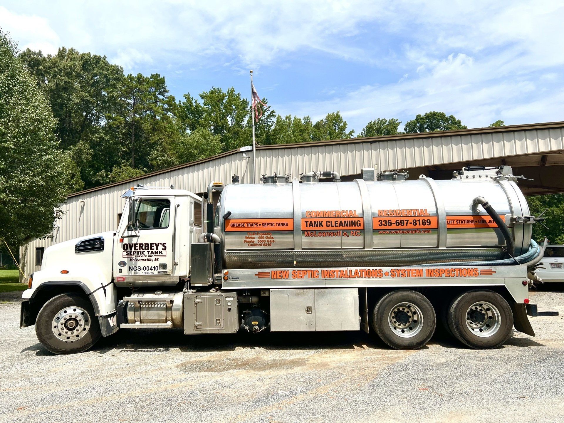 White septic tank truck parked outside a building, with company logo and phone number displayed.
