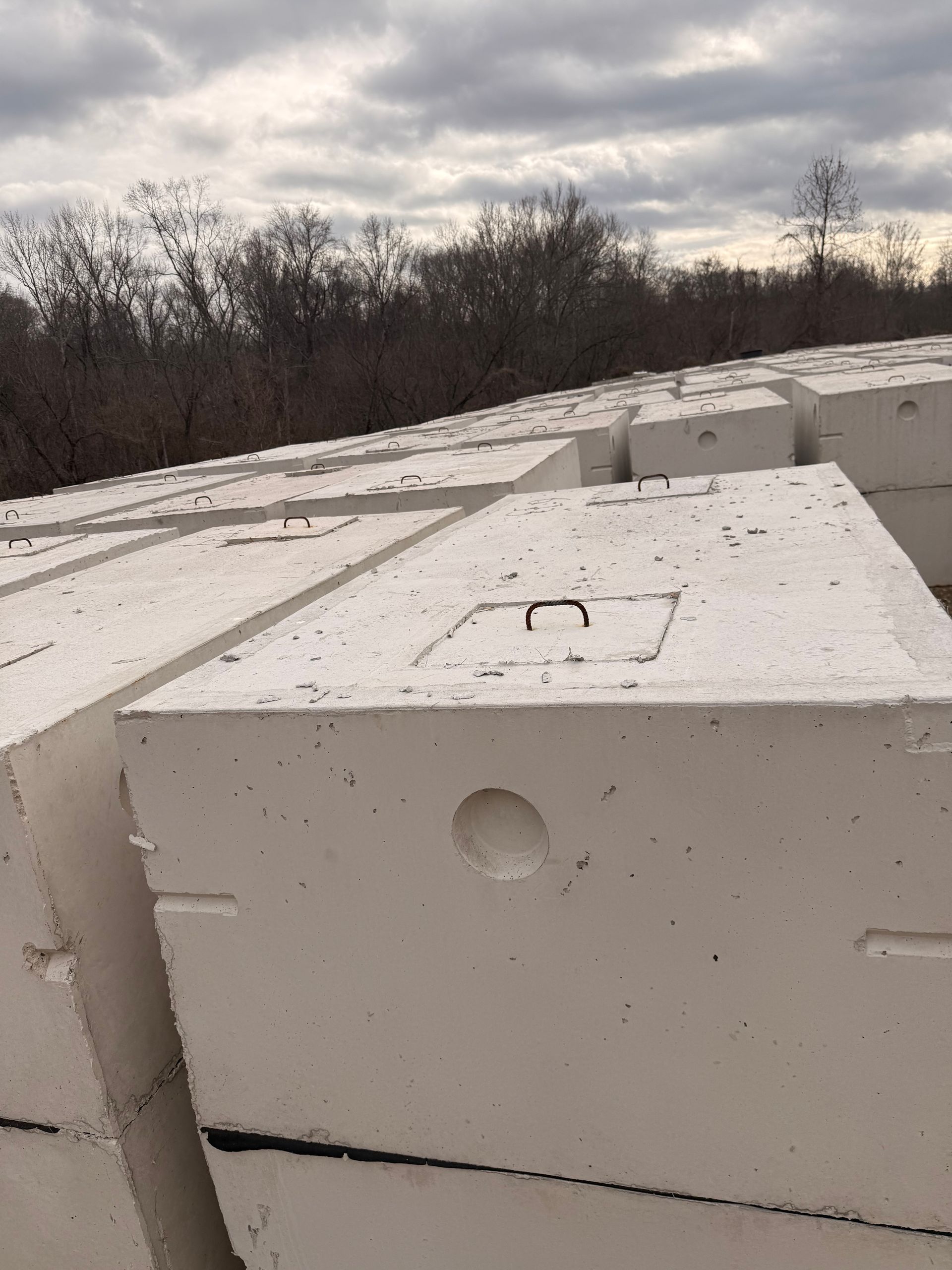 Stacked, rectangular concrete blocks, light grey, with a round hole and metal loop on top. Outdoors, overcast sky.