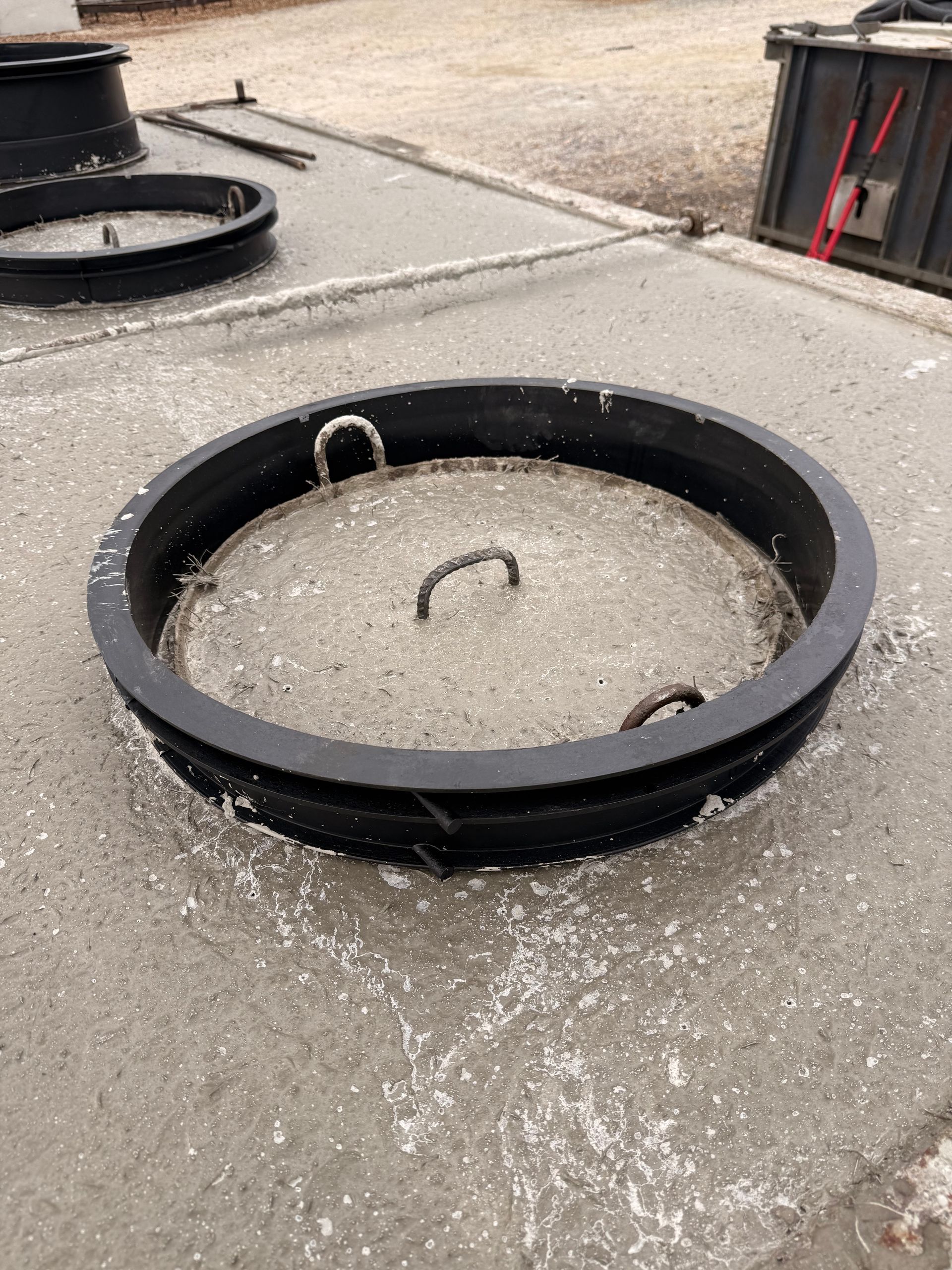 Concrete manhole cover with a black metal frame and three curved handles.