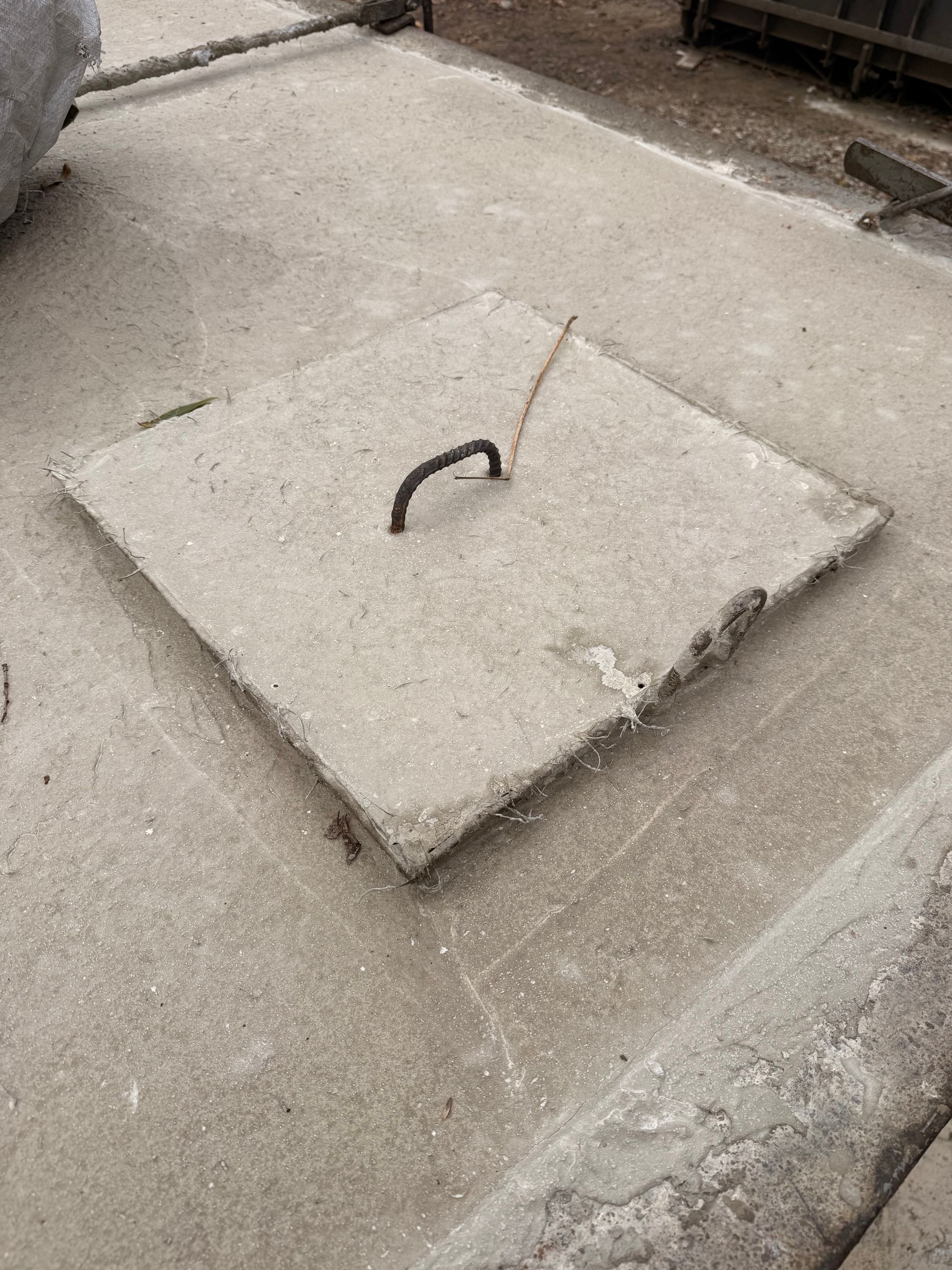 Square concrete cover with metal handle, set in a concrete surface.