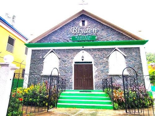 Stone church with green steps, arched windows, and a brown wooden door under a triangular roof.
