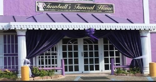 Purple funeral home storefront with awning, white doors, and purple drapes at the entrance