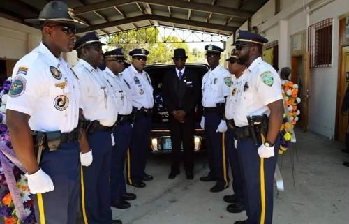 Uniformed officers standing in formation beneath a covered walkway, with a decorated doorway in the background