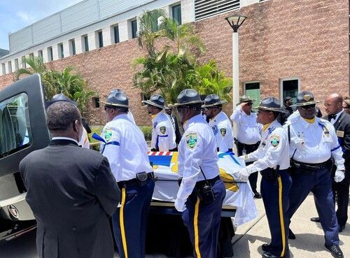 Uniformed officers around a stretcher outside a brick building with emergency vehicles nearby