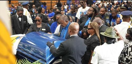 Crowd gathered around a blue coffin in a church, with mourners and uniformed attendees nearby