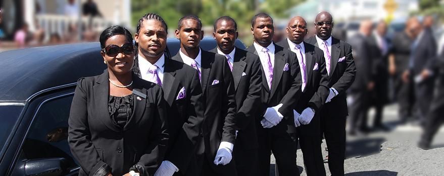 People in black suits and purple ties walking in a formal procession outdoors
