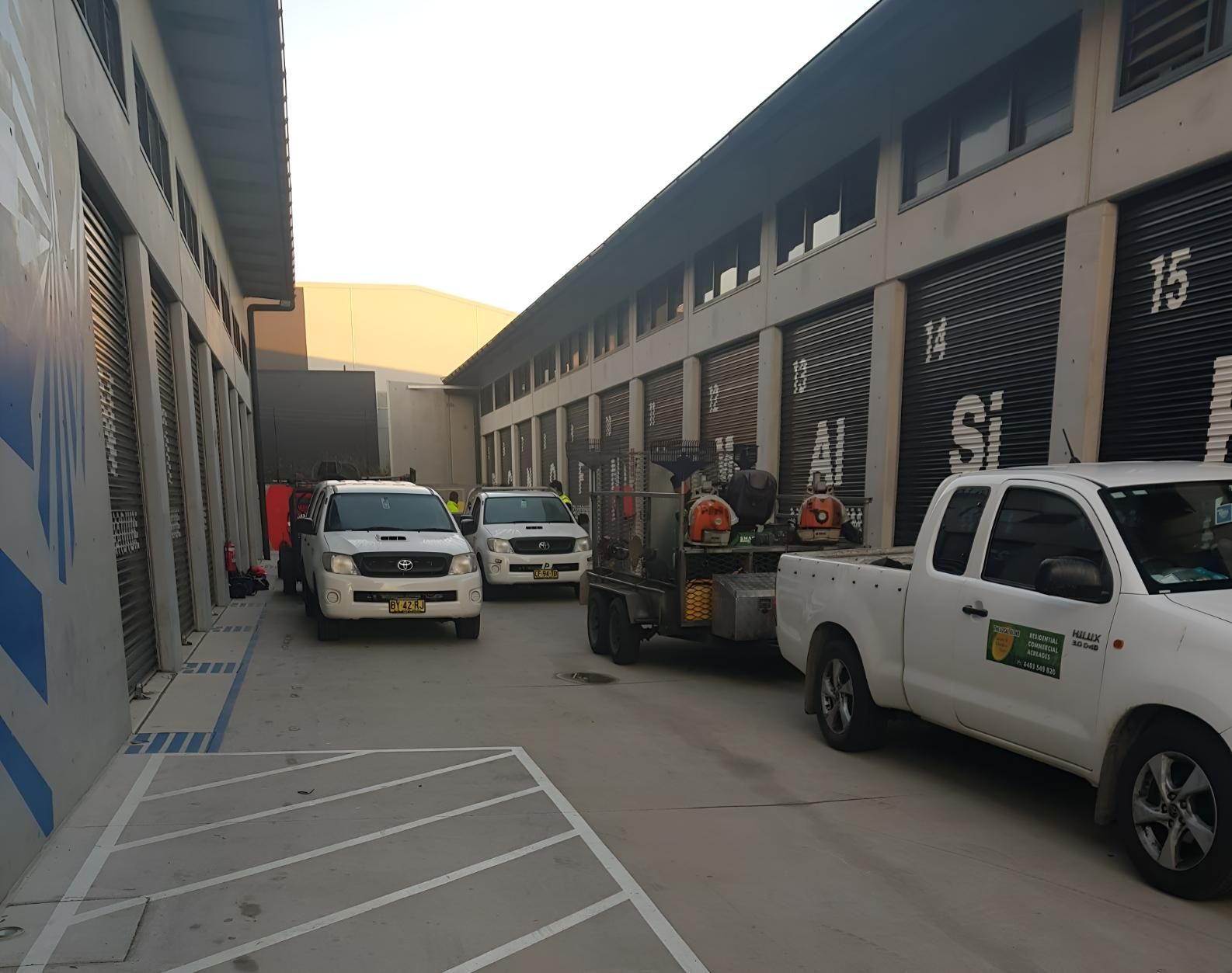 A Row Of Trucks Are Parked In A Parking Lot In Front Of A Building — The Local Bloke Lawn & Garden Care In Warners Bay, NSW