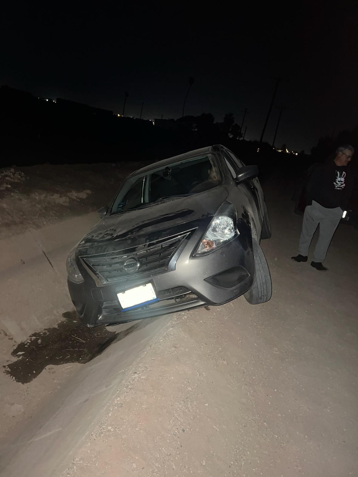 A car is sitting on the side of a dirt road at night.