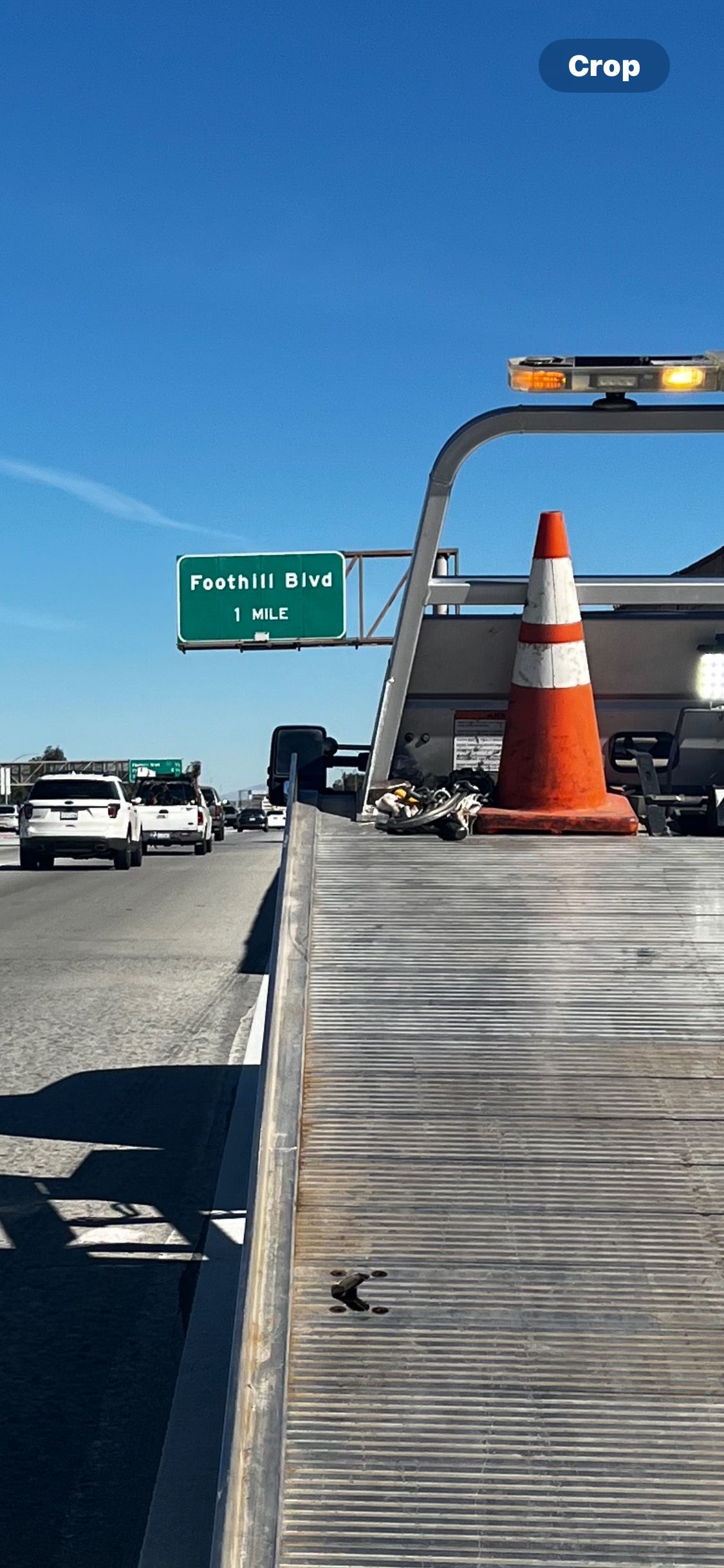 A tow truck is parked on the side of a highway next to a traffic cone.