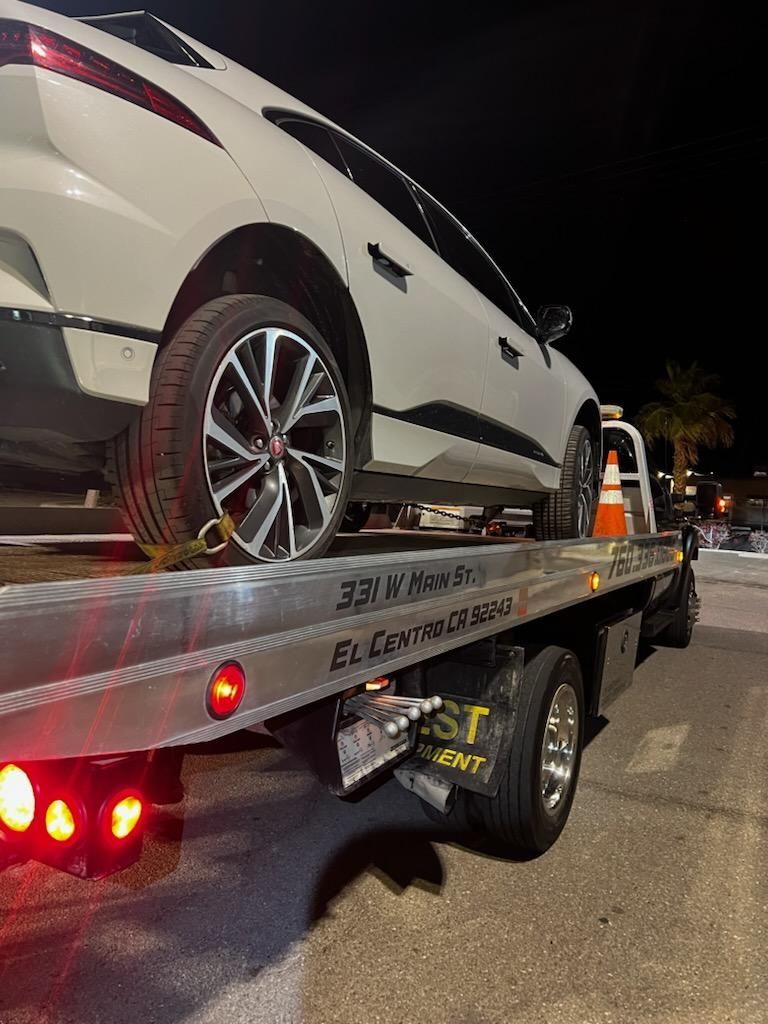 A white car is being towed by a tow truck at night.