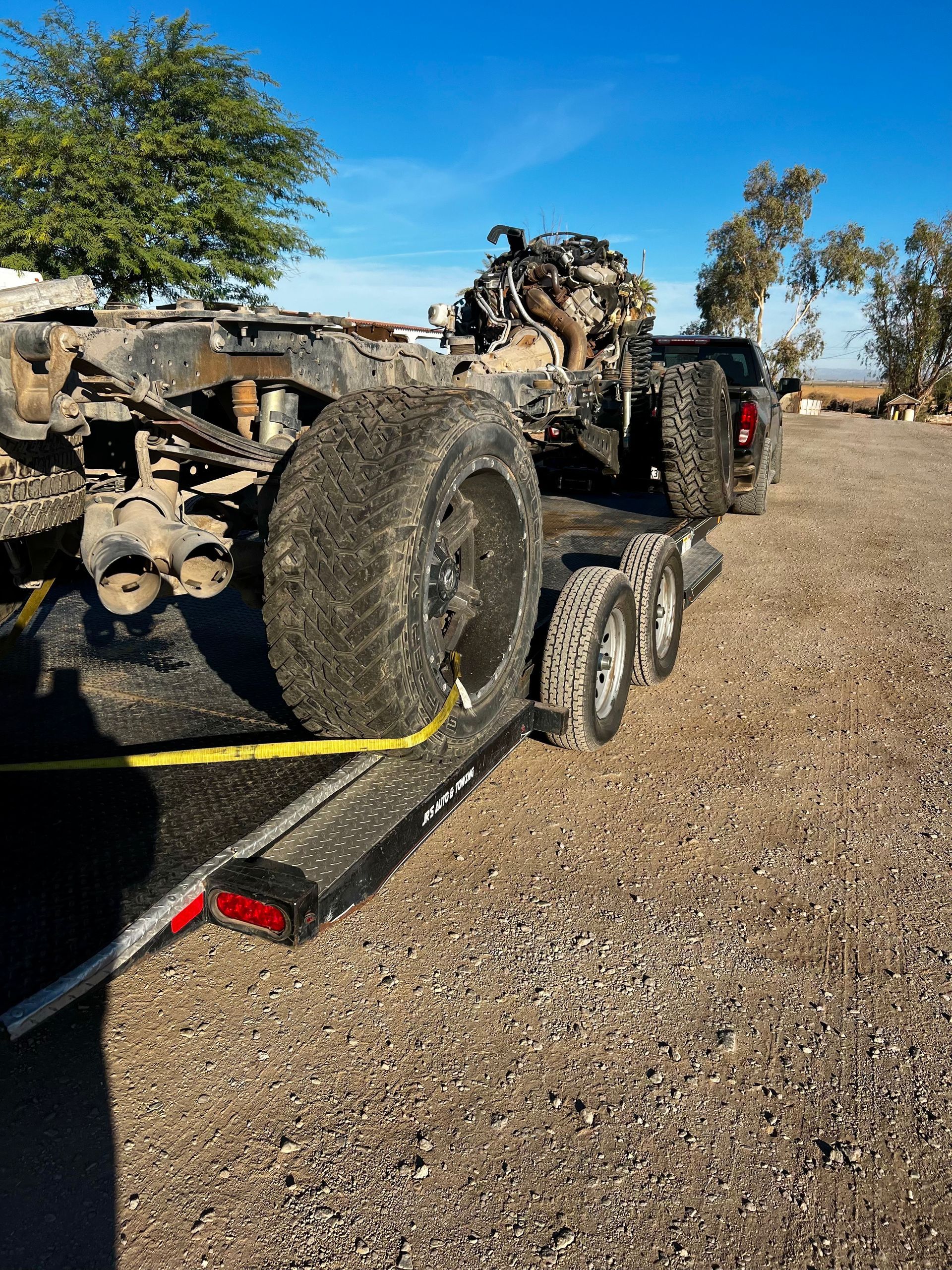 A truck is being towed by a trailer with a large tire on it.