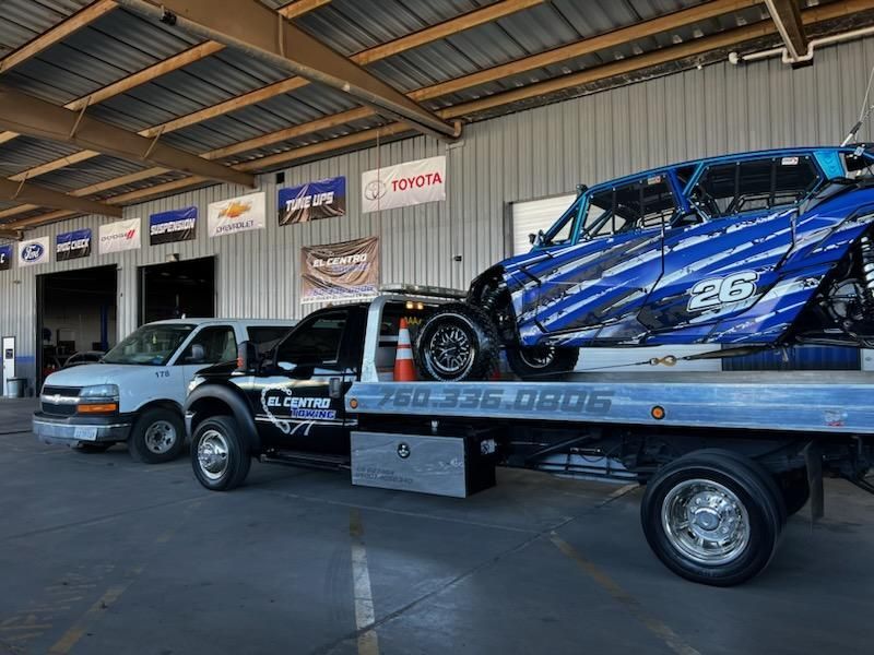 A tow truck is carrying a race car on the back of it.