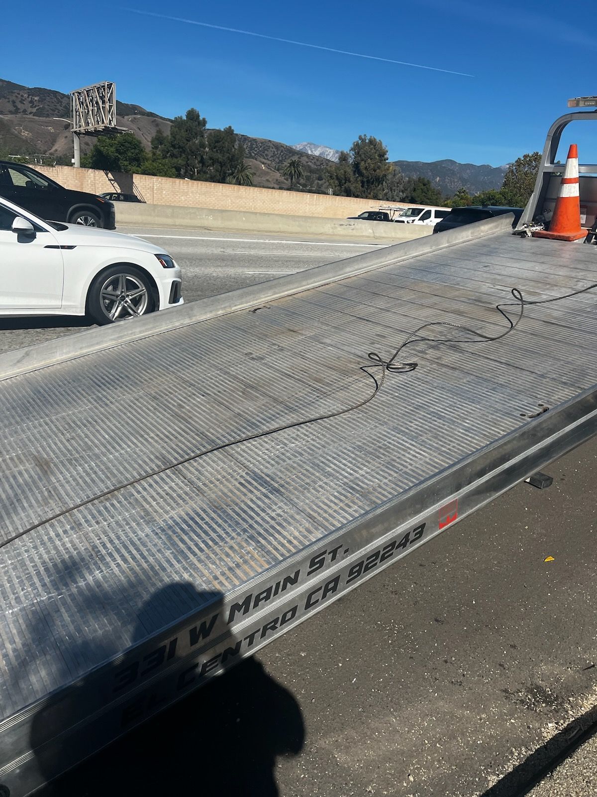 A white car is parked on the side of the road next to a tow truck.