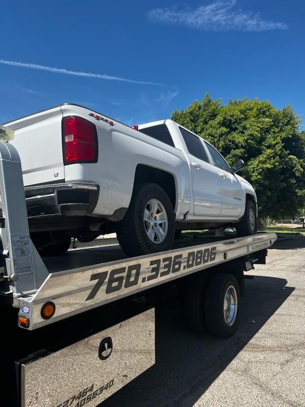 A white truck is sitting on top of a tow truck.