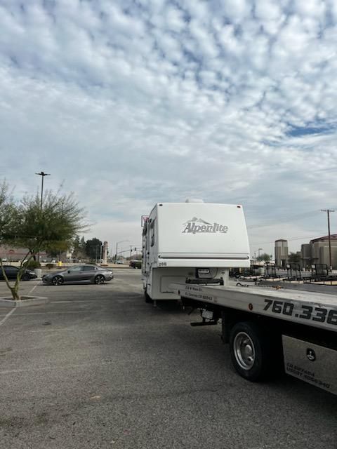 A rv is being towed by a tow truck in a parking lot.
