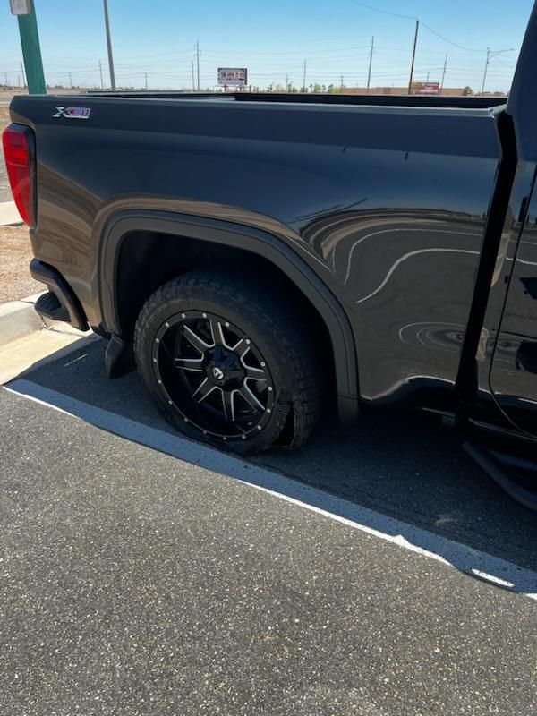 A black truck with a flat tire is parked in a parking lot.