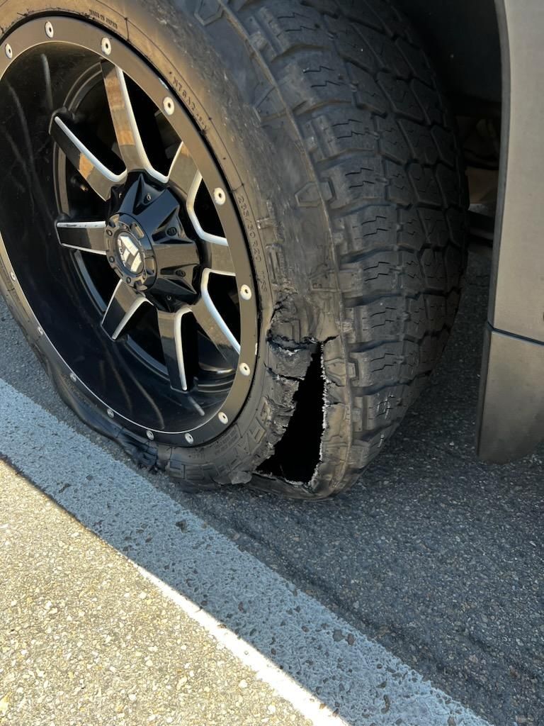 A car with a flat tire is parked on the side of the road.