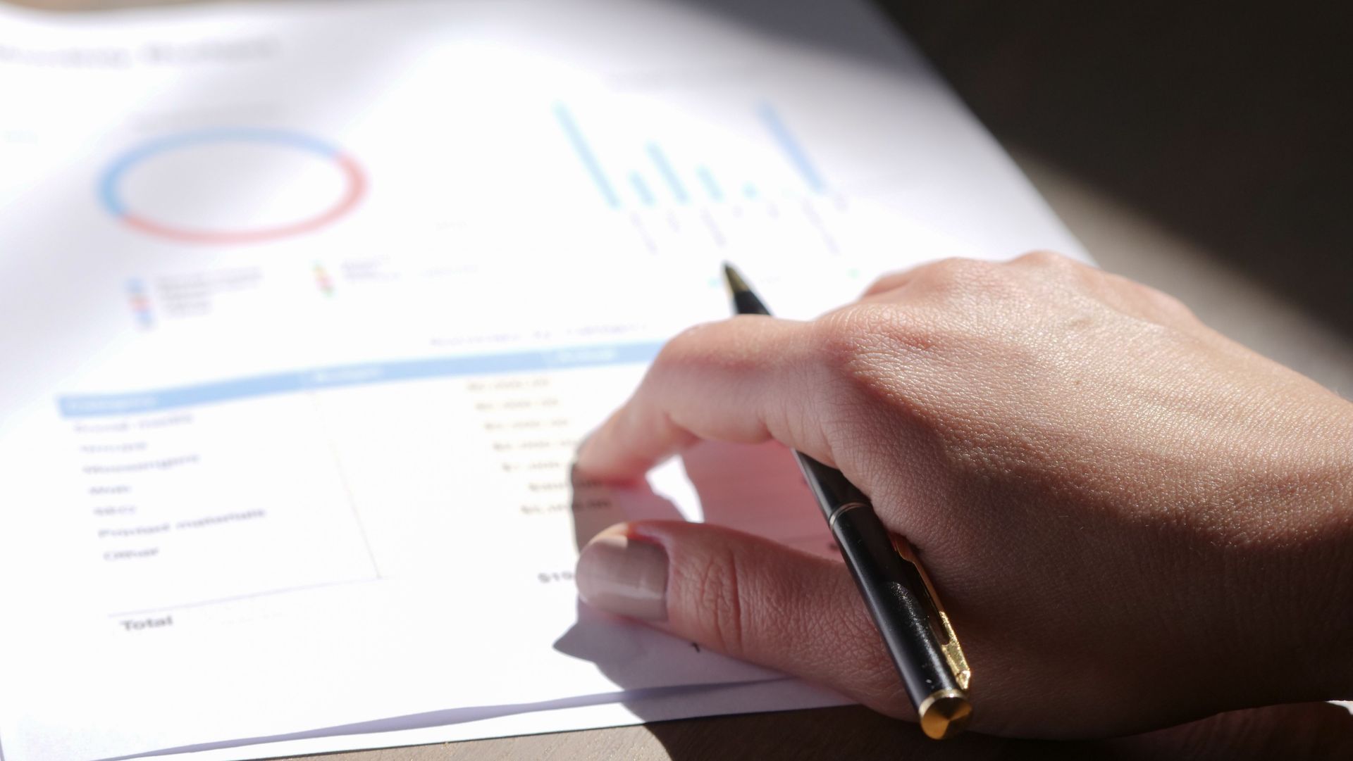 Hand writing on a financial report with charts and tables in the background