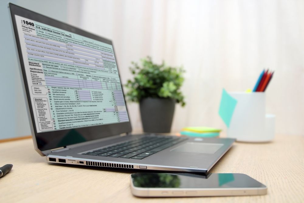 Open laptop on desk with a phone, plant, and pencil cup beside it