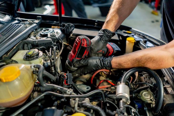 Mechanic using red gloves to work on a car engine in a garage