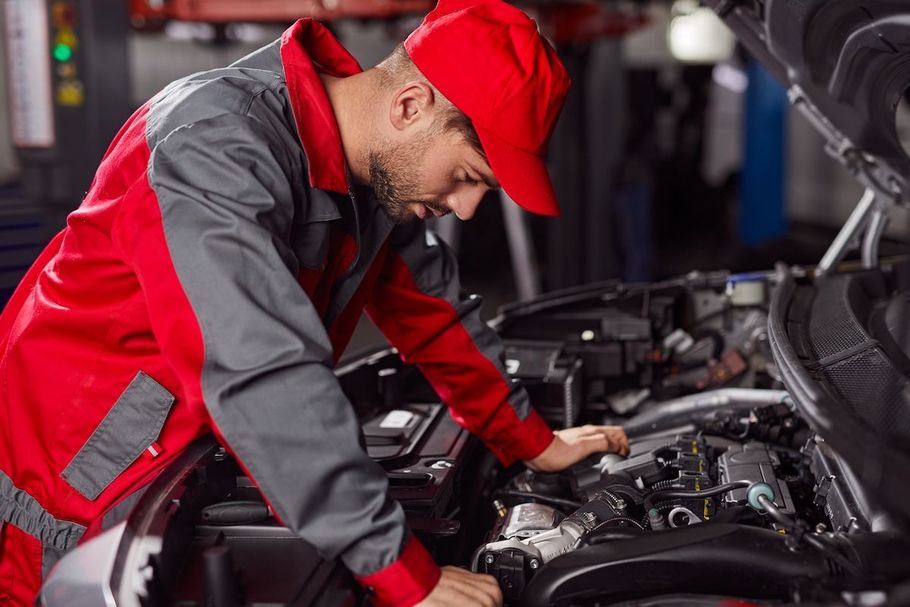 Mechanic in red and gray uniform working under the hood of a car in a garage