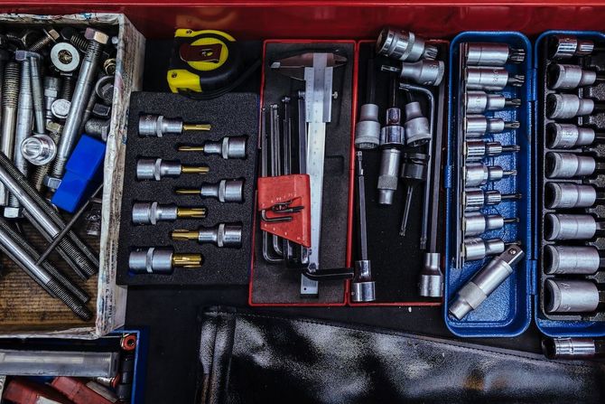Assorted tools and hardware organized in trays, including sockets, drill bits, and wrenches on a work surface.