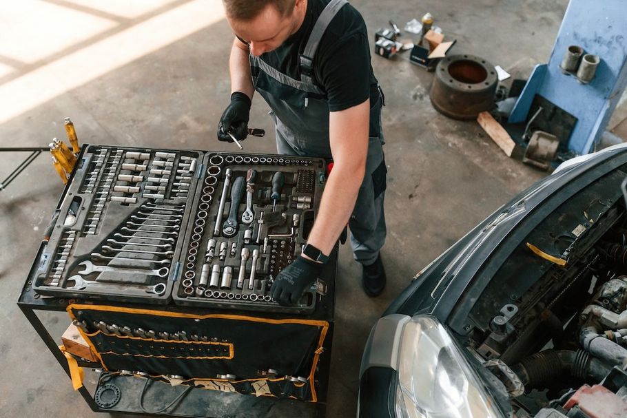 Mechanic working on an engine beside a tool chest and car in a garage