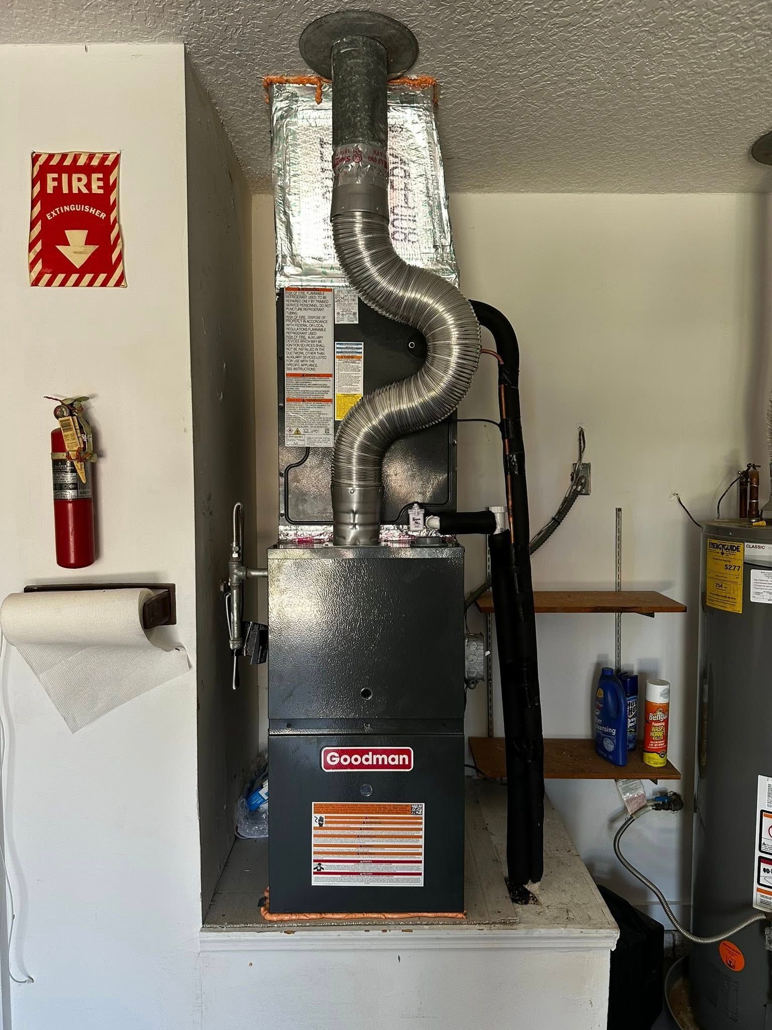 Furnace unit, Goodman brand, with vent, fire extinguisher, and water heater in a utility room.