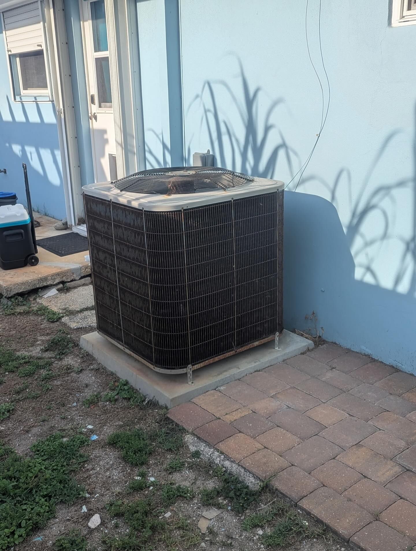 Central air conditioning unit outside a blue building, sitting on a concrete pad.