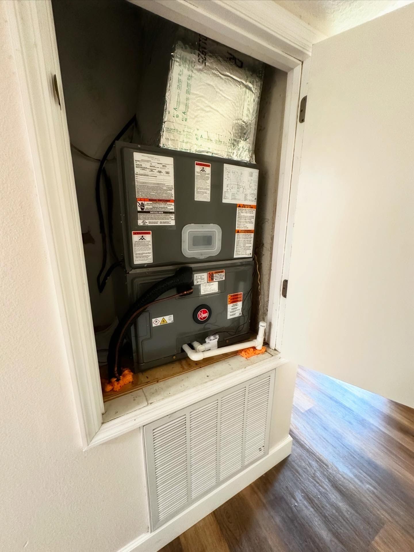 HVAC unit inside a closet, featuring a Rheem brand furnace, with a vent and white door.