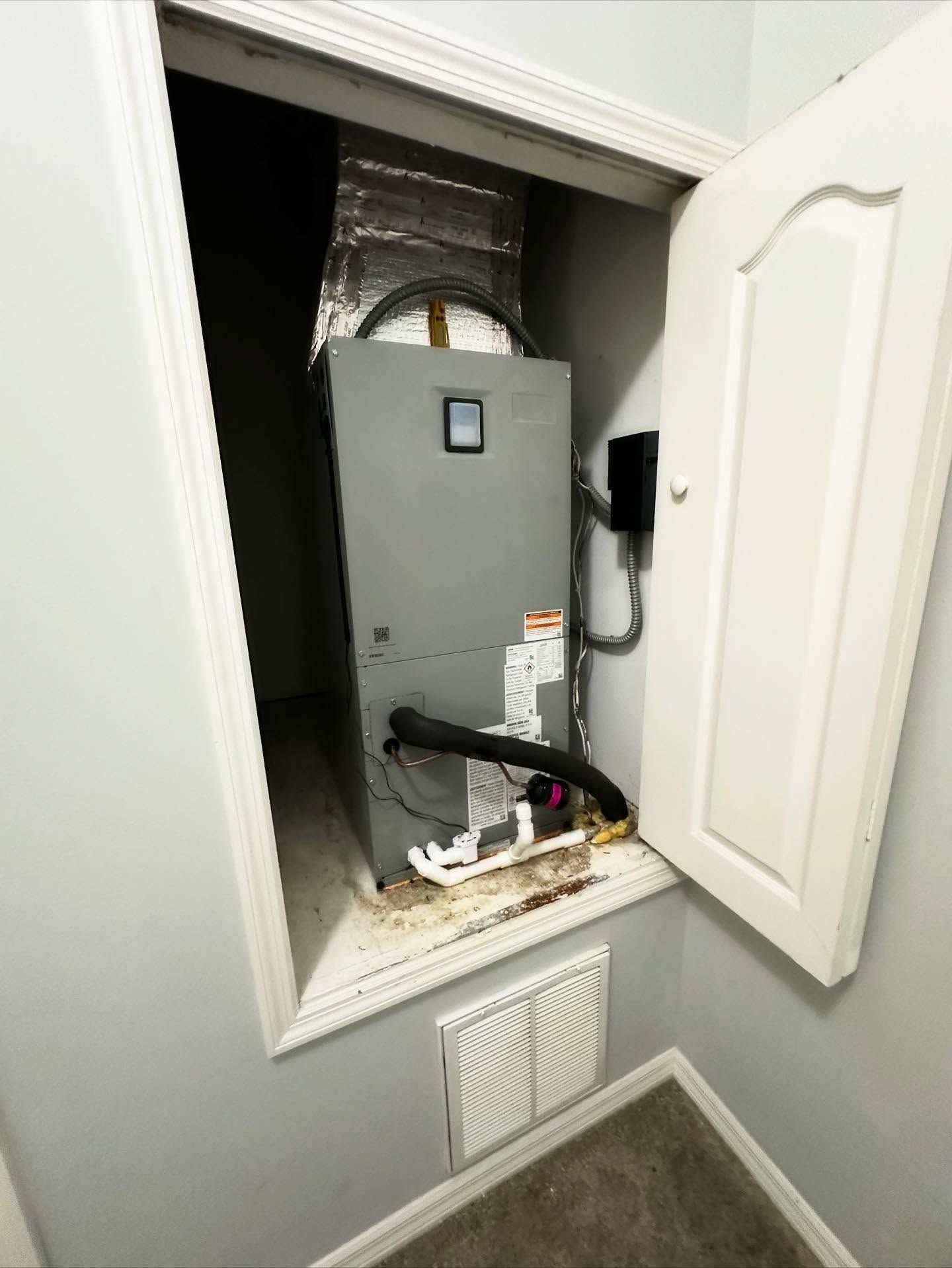 HVAC unit in a small closet, with a partly open white door. Gray walls and carpet.